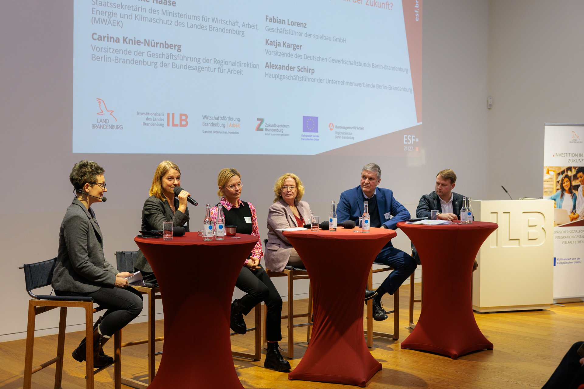 Bild: Podiumsdiskussion mit v.l.n.r. Tina Groll (Moderatorin), Katja Karger (Vorsitzende des Deutschen Gewerkschaftsbunds Berlin-Brandenburg), Carina Knie-Nürnberg (Vorsitzende der Geschäftsführung der Regionaldirektion Berlin-Brandenburg der Bundesagentur für Arbeit), Dr. Friederike Haase (Staatssekretärin des MWAEK), Alexander Schirp (Hauptgeschäftsführer der Unternehmensverbände Berlin Brandenburg), Fabian Lorenz (Geschäftsführer der spielbau GmbH).