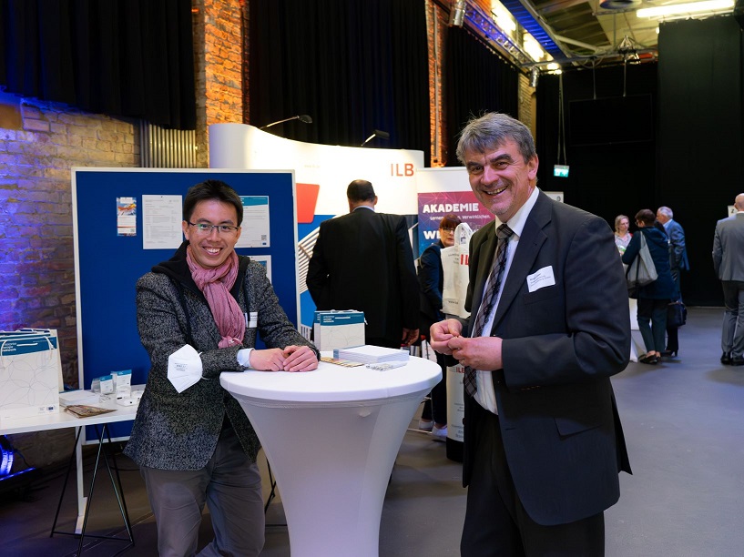 Bild: Dr. Kuang Dai und Holger Zeiser von der WFBB stehen an einem Tisch und lächeln in die Kamera