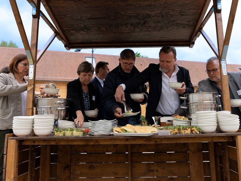 Bild: Mehrere Gäste nehmen sich Essen, das draußen auf einem Buffet aufgebaut ist