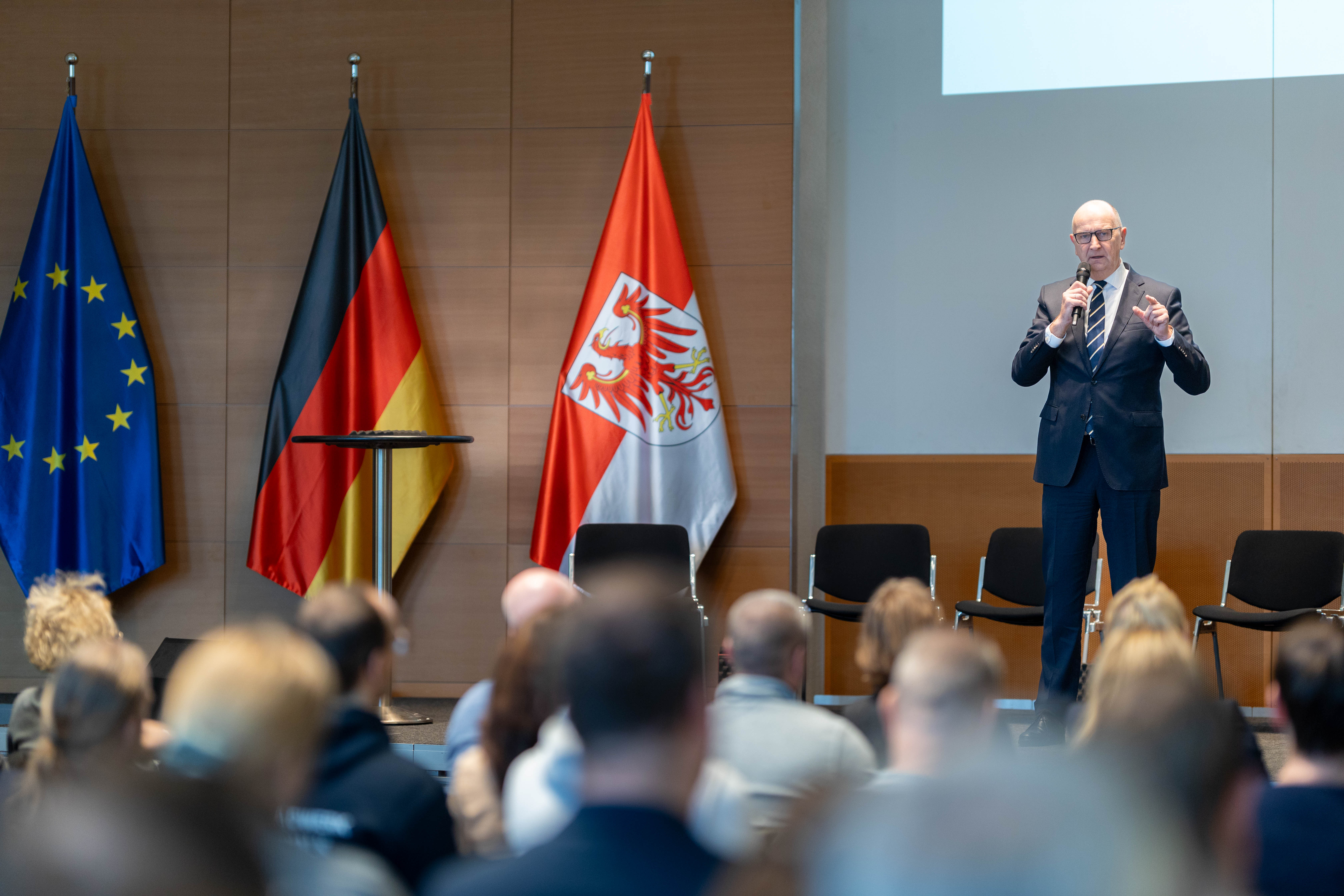 Brandenburgs Ministerpräsident Dietmar Woidke hält eine Rede auf der Bühne, vor ihm sitzen viele Betriebsrätinnen und Betriebsräte.