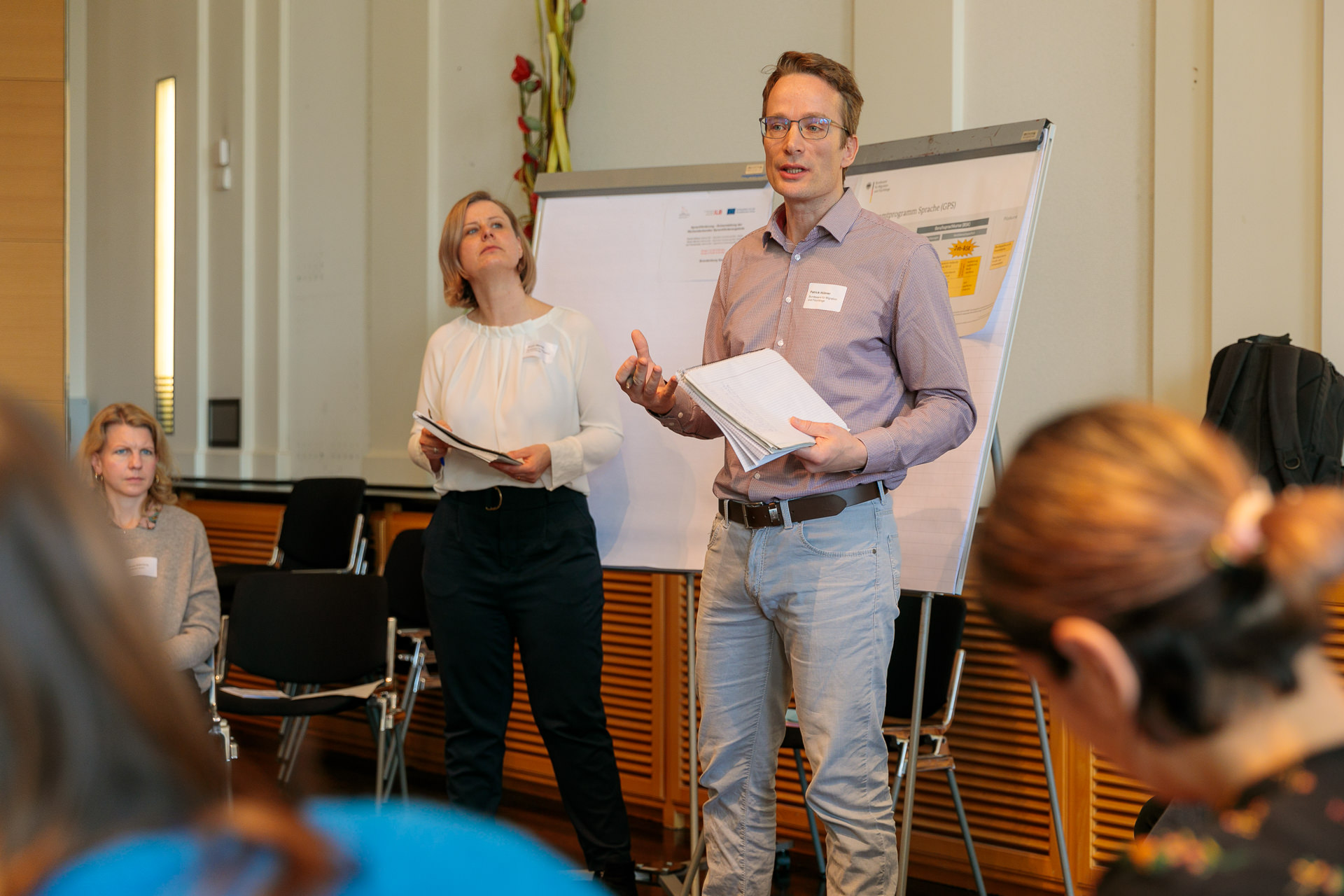 Bild: Vor einem Flipchart stehend spricht Patrick Hübner zu den Teilnehmenden, links neben ihm steht Kristin Werner.