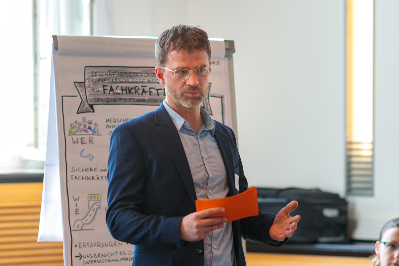 Bild: Torsten Künzel steht vor einem Flipchart und spricht zu den Teilnehmenden der Table-Session.