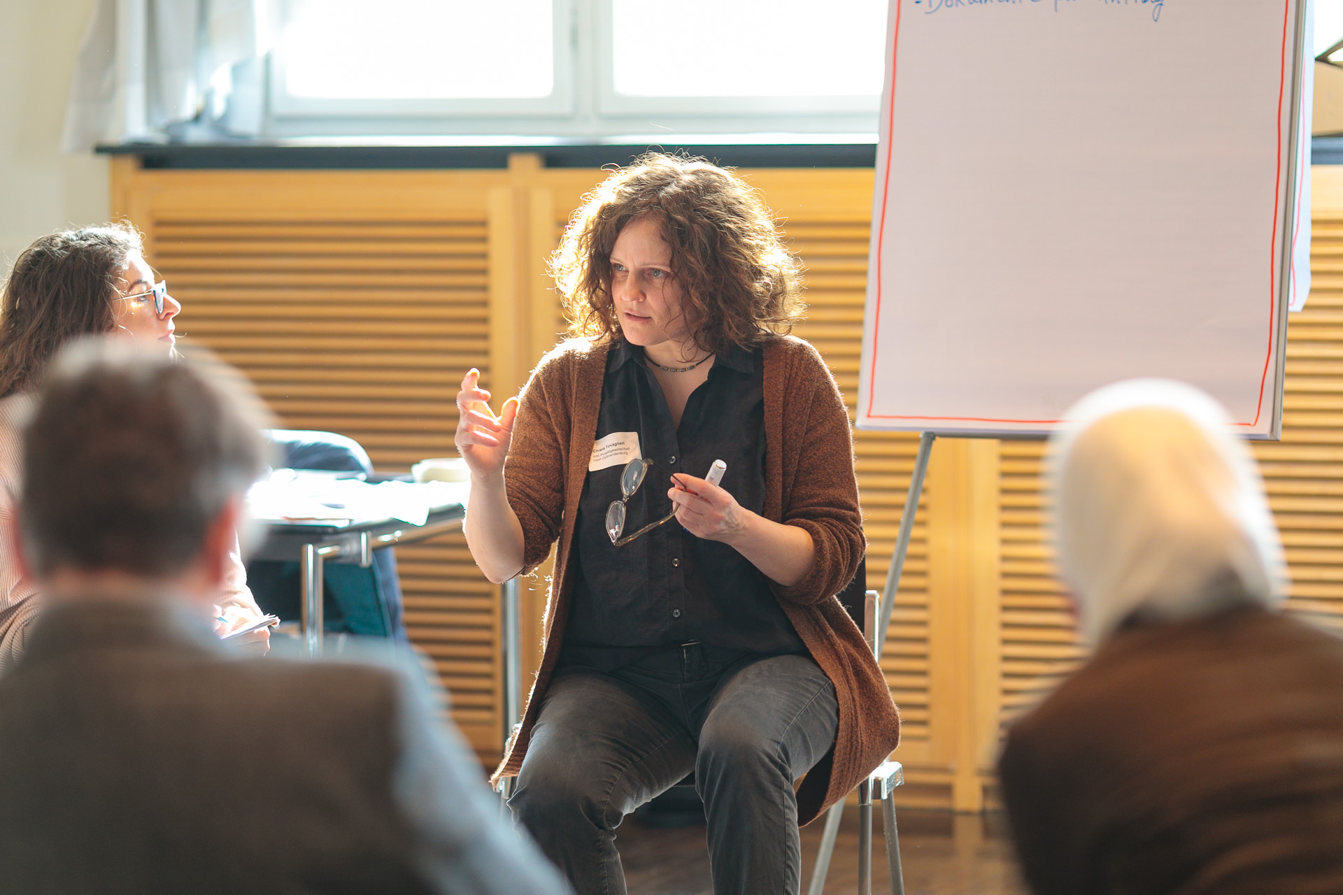 Bild: Chiara Tovaglieri sitzt neben einem noch leeren Flipchart und spricht zu den Teilnehmenden der Table-Session.