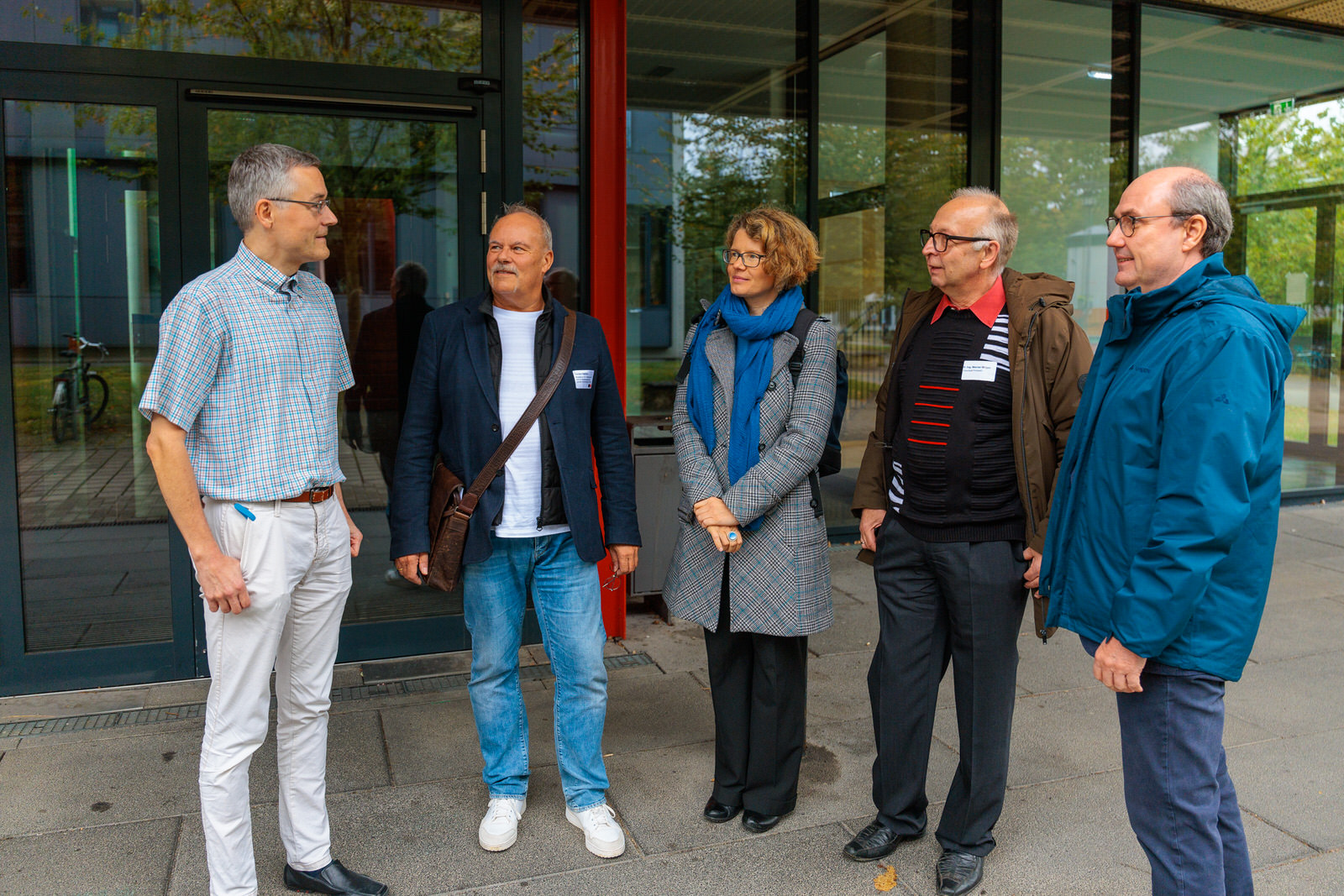 Bild: Mehrere Menschen stehen vor der Glasfront/dem Eingang des Institut für Physik und Astronomie und schauen zu Werner Wirges (links).