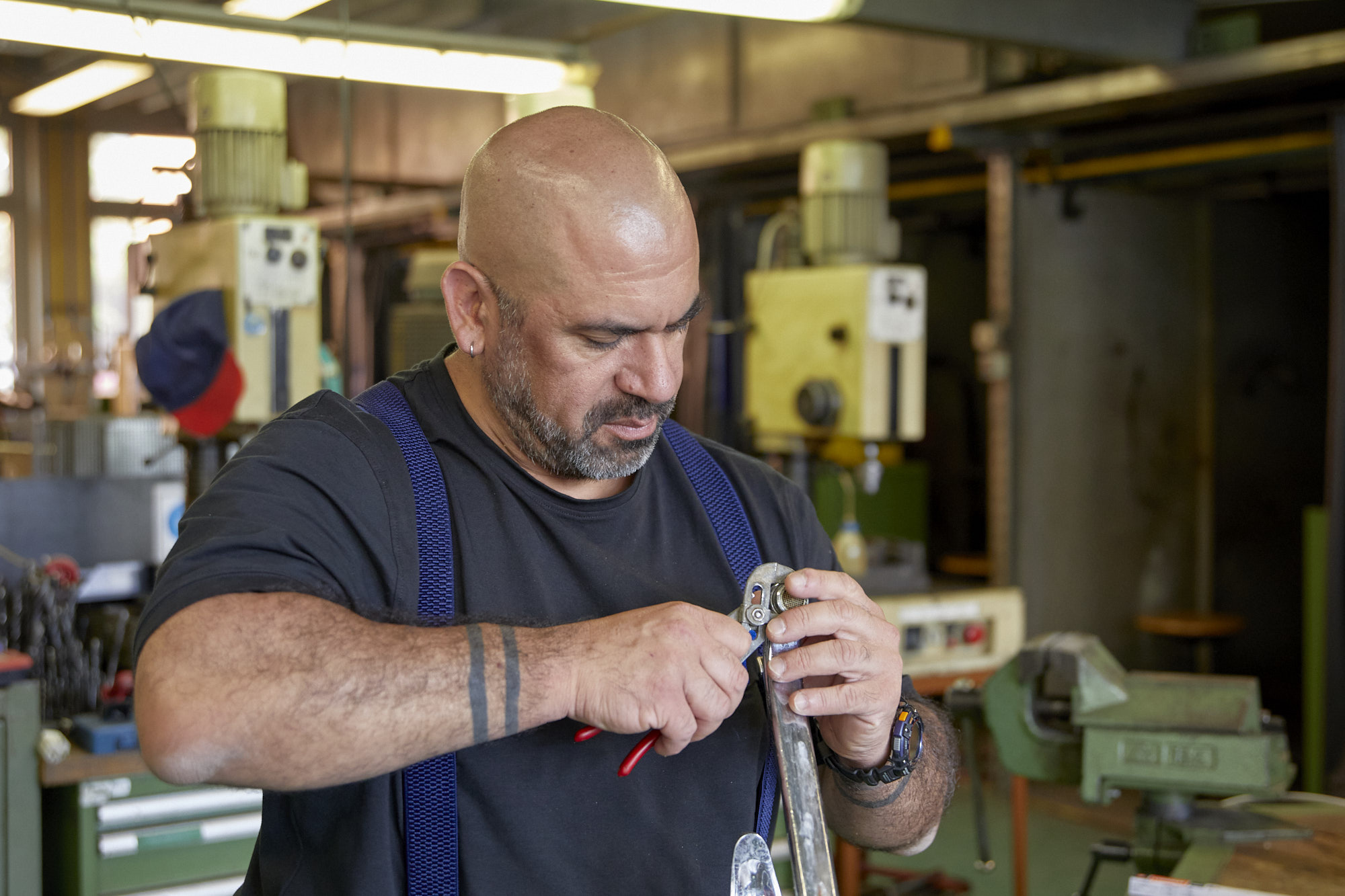 Mann im Blaumann steht in einer Werkstatt mit einer Zange in der Hand und montiert etwas.