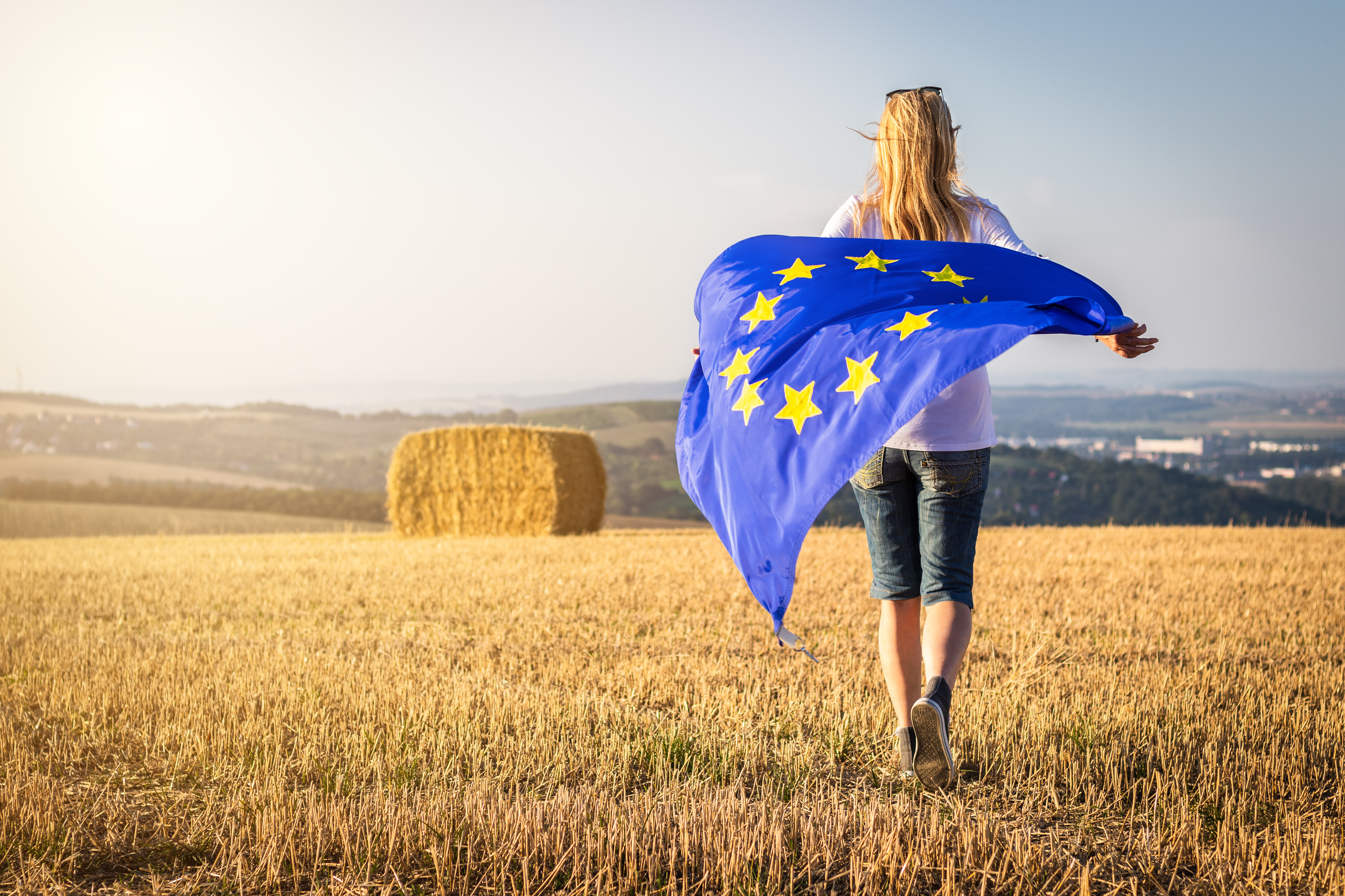 Eine Frau trägt eine EU-Flagge und läuft über ein Feld.