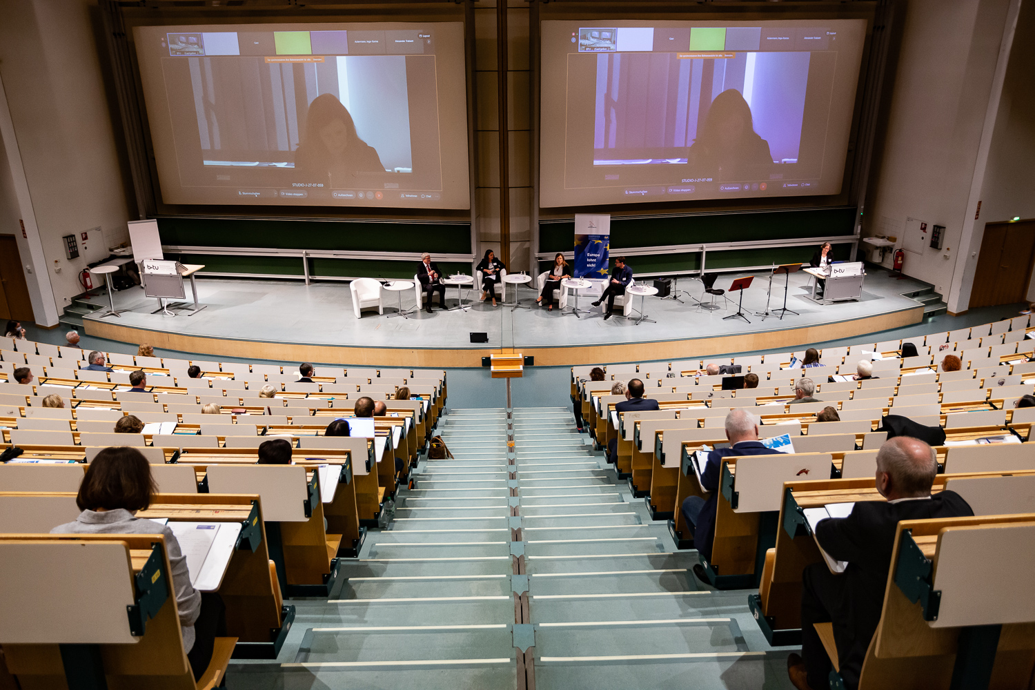 Bild: Das Bild zeigt die Podiumsdiskussion, aufgenommen von den Rängen des Audimax aus, mit Blick auf die Bühne.