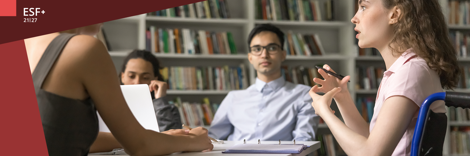 Mehrere junge Menschen sitzen am Tisch und hören einer jungen Frau im Rollstuhl zu