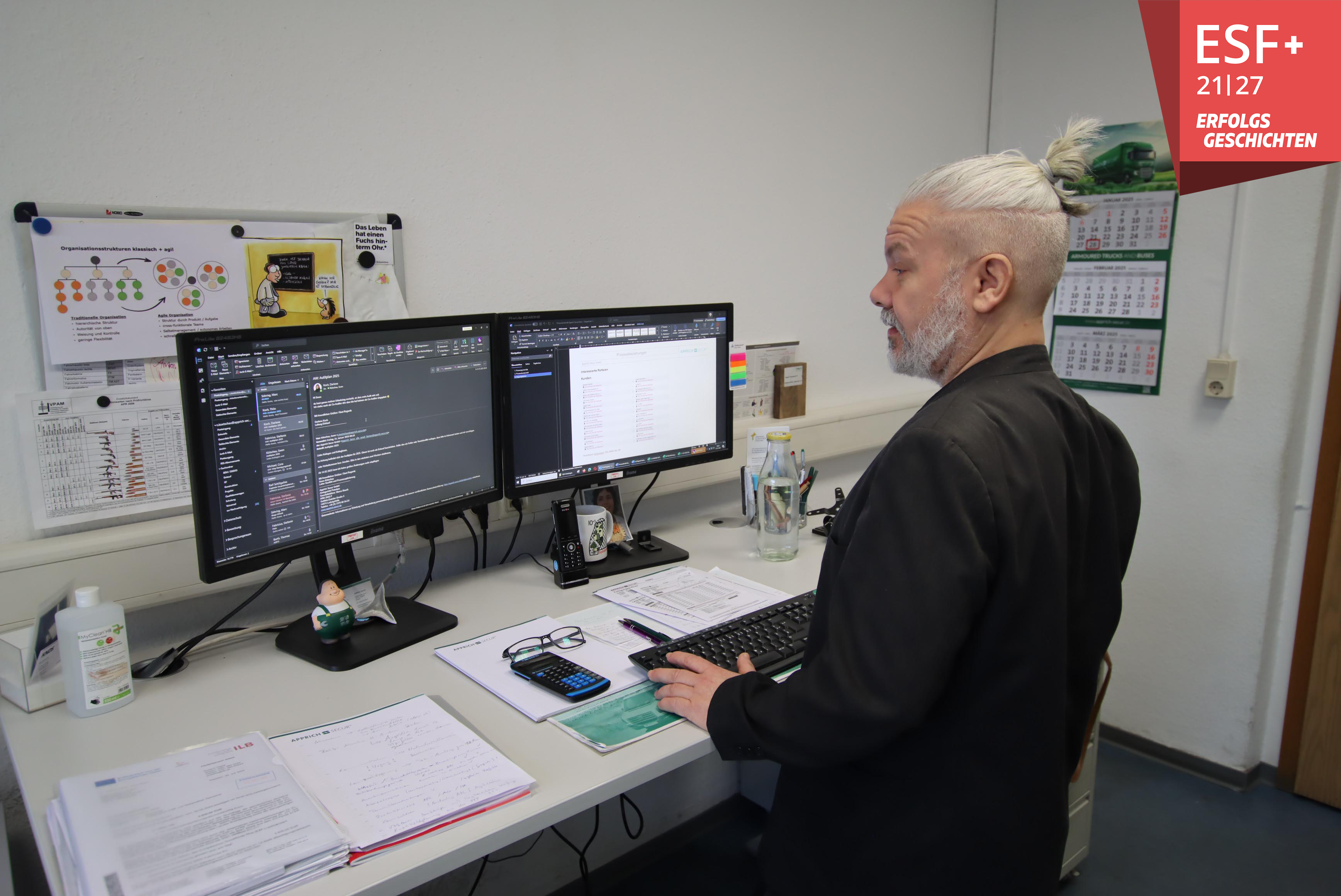 Sven Kötschau steht vor seinem Arbeitsplatz, auf dem zwei Monitore und etliche Büromaterialien stehen.