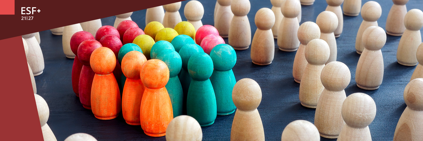 Eine größere Anzahl kleiner Holzspielfiguren, die meisten davon farblos, im Vordergrund eine eng zusammenstehende Gruppe bunter Holzspielfiguren.