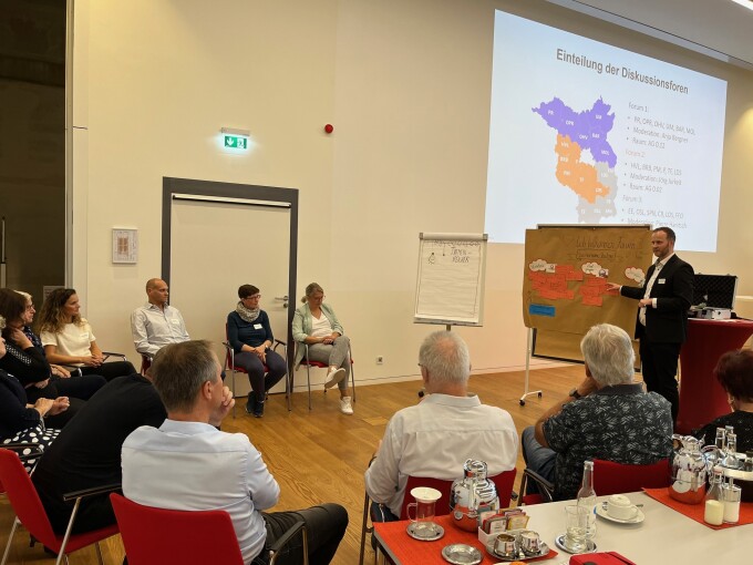 Pierre Hanitsch von der WFBB steht an einer Metaplanwand mit farbigen Kärtchen, davor sitzen im Halbkreis Teilnehmende der Diskussionsrunde.