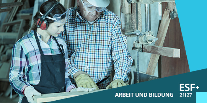 Eine junge Frau in Arbeitskleidung mit Gehörschutz und Schutzbrille wird von einem älteren Mann mit Helm und Schutzbrille an einem Bohrer angeleitet.