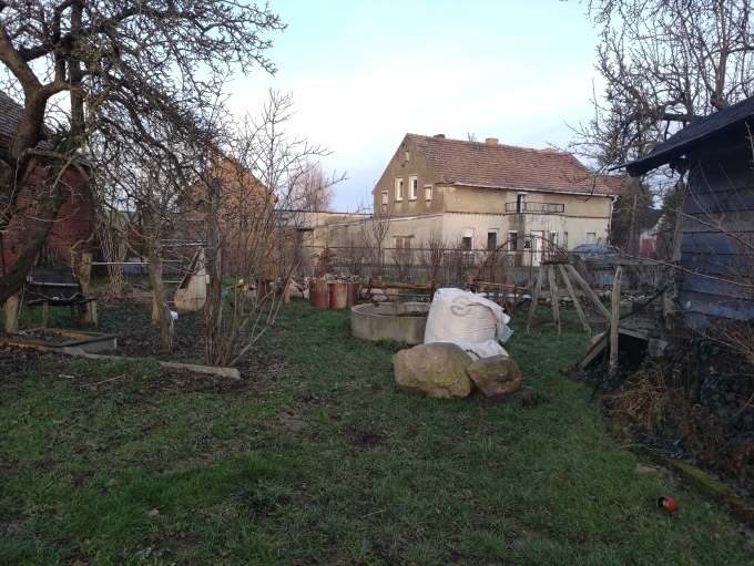 Kleiner Garten mit Gras, Sträuchern und einem Schuppen, im Hintergrund stehen Einfamilienhäuser.