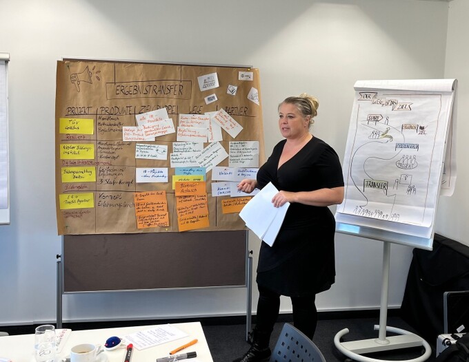 Eine Teilnehmerin des Workshops steht an einer Metaplanwand, auf der viele Post-its hängen und Ergebnisse schriftlich festgehalten sind.