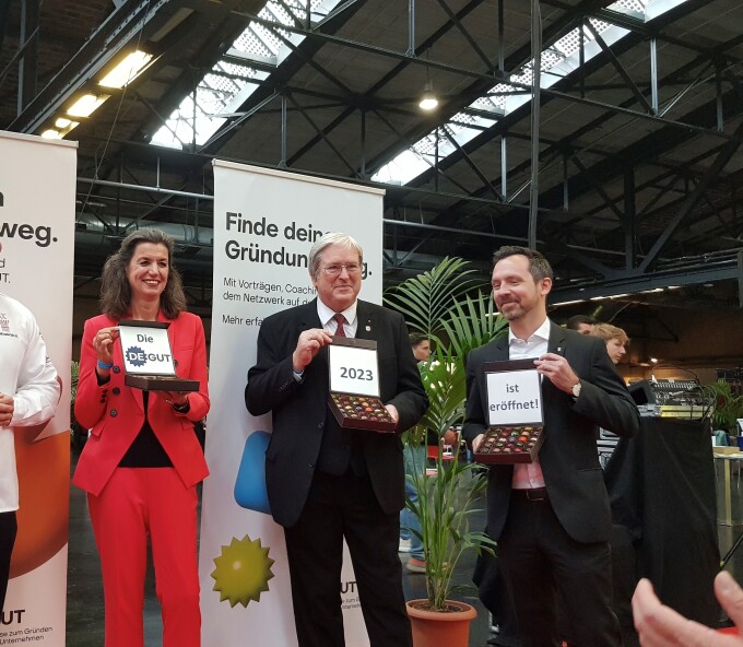 Dr. Sabine Hepperle, Dr. Severin Fischer und Prof. Dr.-Ing. Jörg Steinbach halten Pralinenschachteln hoch, welche die Worte "Die deGUT 2023 ist eröffnet" abbilden.