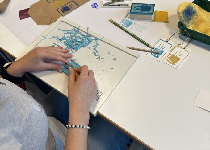 Nahaufnahme von zwei Händen, die auf einer Bastelunterlage einen Stempel schnitzen.
